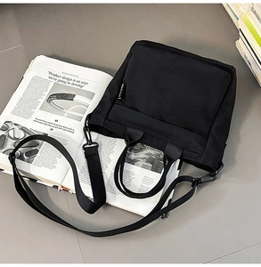 Flat lay of black nylon tote bag with wide strap and side woven label on grey background