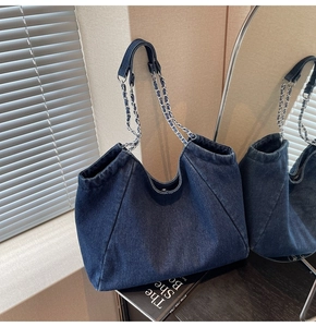 Detail of dark blue denim tote bag featuring chain straps and visible stitching texture