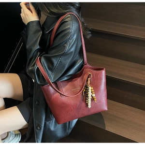 Detail view of burgundy leather tote bag with gold logo and vintage beaded charm