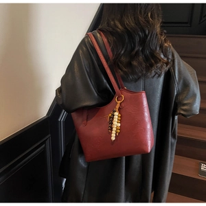 Detail of burgundy leather tote bag with unique colorful wooden bead charm and dual straps