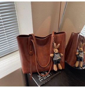Brown leather tote bag detail with cute bunny charm in soft window light setting