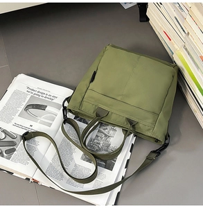 Olive green nylon tote bag featuring adjustable canvas shoulder strap and front zipper pocket