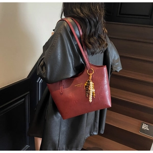 Detail of burgundy vintage tote bag with wooden bead charm on a black leather coat