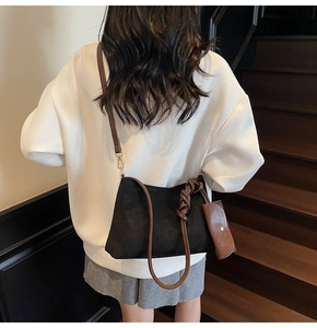 Detail of black suede tote bag featuring brown leather strap and mini charm pouch accessory