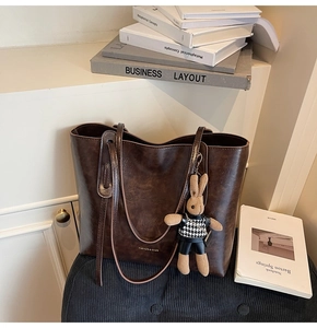 Detail of vintage brown tote bag with glossy leather texture and cute rabbit charm