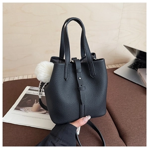 Close-up of black lychee grain leather bucket bag with plush charm and pearl chain