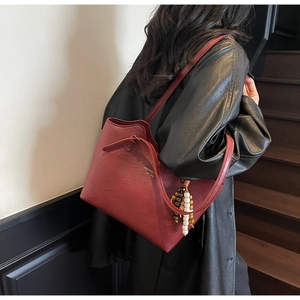 Detail of burgundy leather tote bag with gold logo and colorful beaded tassel charm