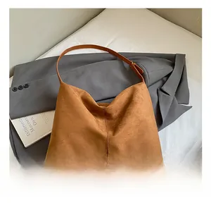 Detail of a brown suede tote bag with leather straps on a grey blazer backdrop