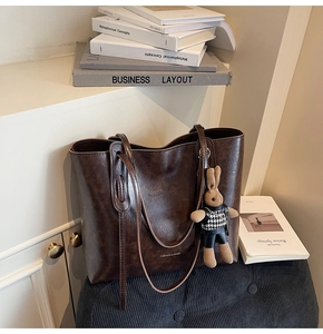 Detail of vintage brown leather tote bag with doll pendant on a soft black cushion