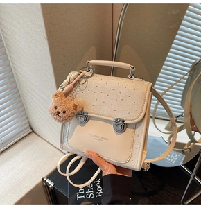 Detail of cream white leather backpack with metal buckles and cute plush bear charm