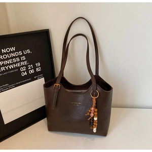 Detail of dark brown leather tote bag with brand logo and wooden beaded tassel charm