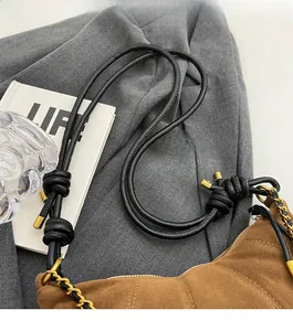 Detail of the brown suede handbag showing a knotted black leather strap and gold chain