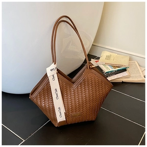 Detail of a brown woven tote bag featuring a V-shaped top and white logo ribbon strap