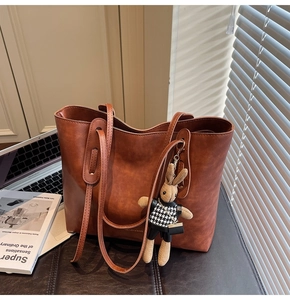 Detail of vintage brown faux leather tote bag with rabbit charm on a desk workspace