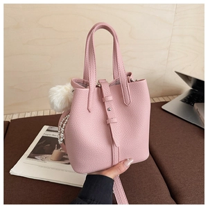 Detail of pink lychee leather bucket bag with pearl chain and white pompom charm accessory