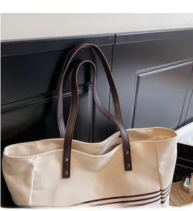 Close-up of durable canvas tote bag featuring brown leather handles and metal rivets
