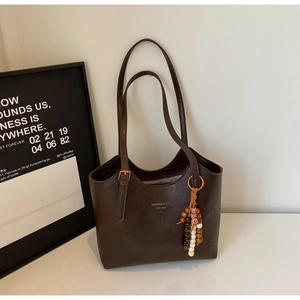 Detail of dark brown tote bag with gold brand logo and colorful wooden bead tassel