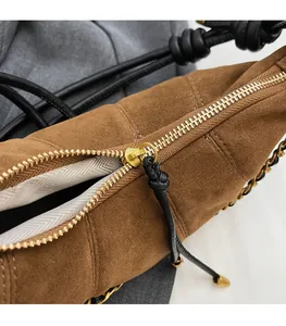 Detail of smooth gold zipper and beige herringbone lining on brown suede croissant bag