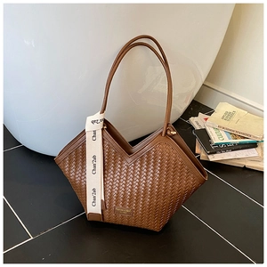 Close-up of brown woven tote bag with V-shaped opening and decorative white ribbon