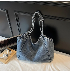 Detail of blue washed denim hobo bag featuring silver metal chain strap on a white table