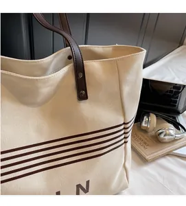 Detail of canvas tote bag with brown leather handles and striped minimalist design