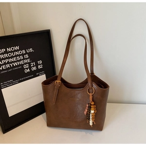 Detail of dark brown leather tote with gold logo and colorful wood bead charm