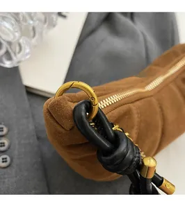 Detail of brown suede handbag with gold ring buckle, zipper, and black leather knot strap