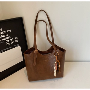 Detail view of a vintage brown tote bag with smooth texture and decorative bead charm