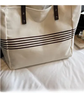 Detail of canvas tote bag featuring brown stripes, leather handles, and metal rivet accents
