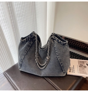 Detailed view of dark blue washed denim tote with silver chain handles on leather surface