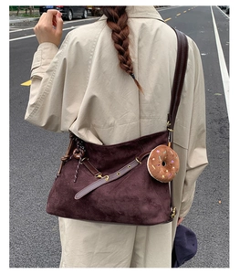 Close-up of deep coffee suede tote bag with plush donut charm on a beige coat model