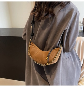 Detail of brown suede croissant bag with metal chain strap worn over a grey blazer