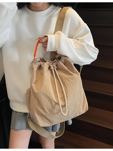 Zaino in tela beige con tracolla arancione indossato da modella su una scala