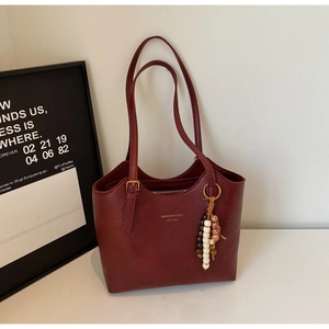 Close-up of vintage burgundy tote bag with gold logo and beaded accessory detail