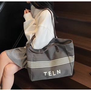 Grey canvas tote bag with long brown leather straps worn on a stylish wooden staircase