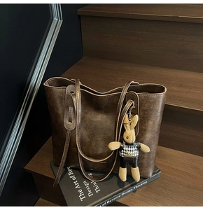 Detail of vintage brown leather tote bag with long straps and cute bunny charm on books
