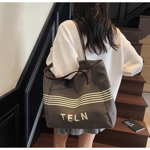 Detail of taupe canvas tote bag with white stripes and brown leather handles on stairs