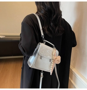 Close-up of silver-grey textured leather backpack with buckles and bear charm detail
