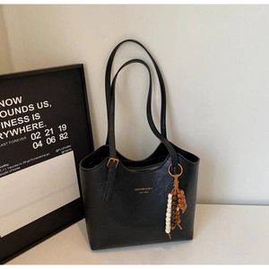 Detail of a black faux leather tote bag featuring a gold logo and a vintage beaded pendant