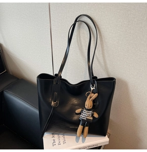 Detail of a black leather tote bag with a brown rabbit charm on top of a design book