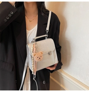 Detail of silver textured leather handbag featuring metal handle and brown teddy charm