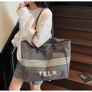 Detail of grey canvas tote bag with white stripes and brown leather handles on shoulder