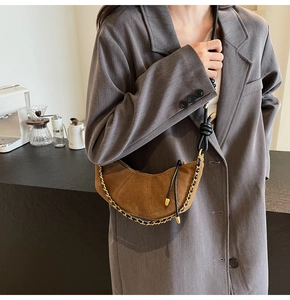 Detail view of brown suede croissant bag with woven strap and gold chain on model