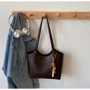 Detail of dark brown leather tote bag with gold logo and vintage beaded tassel