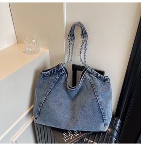 Close-up of washed blue denim tote bag with silver chain strap on a black suitcase