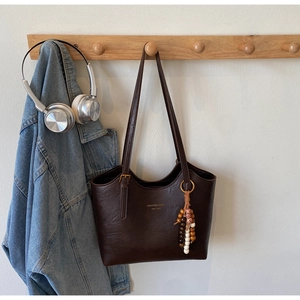 Close-up of vintage brown tote bag with colorful beaded charm on a wall hook