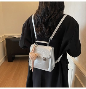 Silver mini backpack with bear charm and top handle worn over a black coat