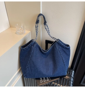 Close-up of vintage denim tote bag with silver chain straps leaning on a suitcase