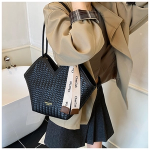 Detailed view of black woven tote bag featuring gold logo plate and patterned scarf accent