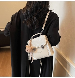 Close-up of white PU leather mini backpack featuring embroidery and a cute bear charm
